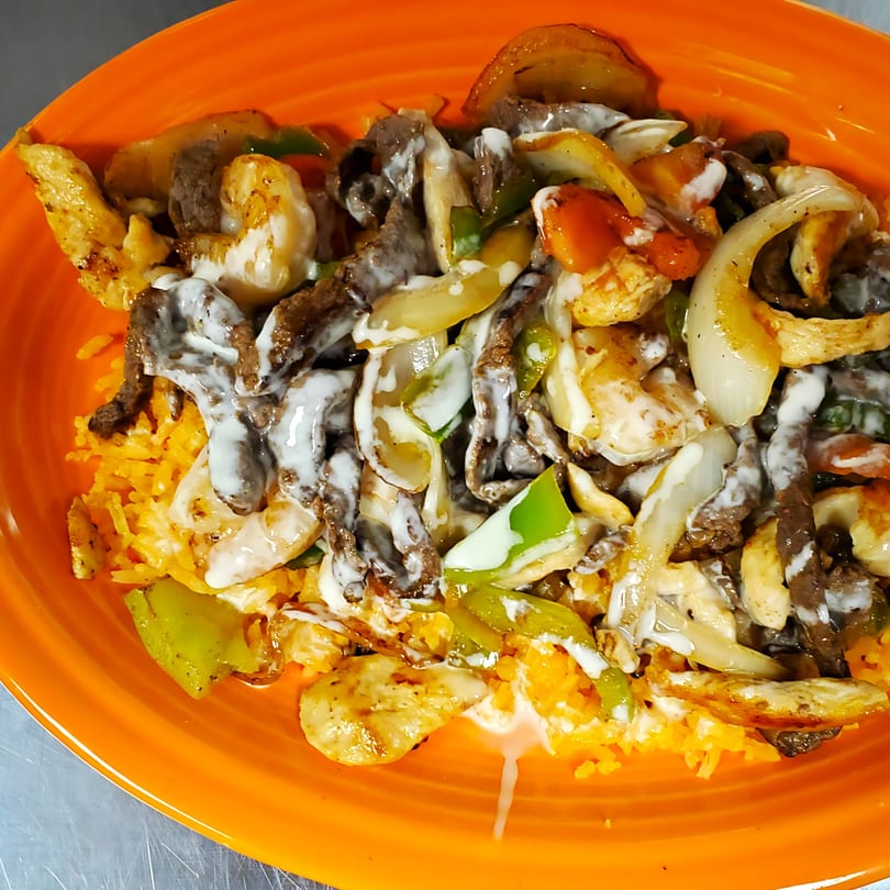 Mexican fajita dish with chicken, beef, shrimp, onions, peppers, and crema over rice.