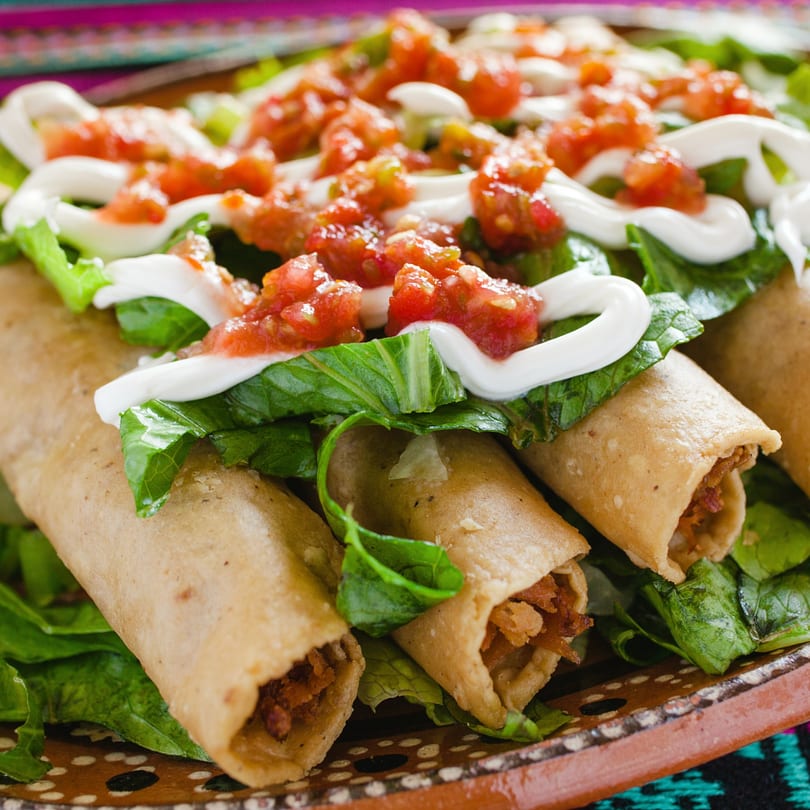 Crispy taquitos from EL SAZÓN BAR & GRILL, topped with fresh lettuce, salsa, and crema.