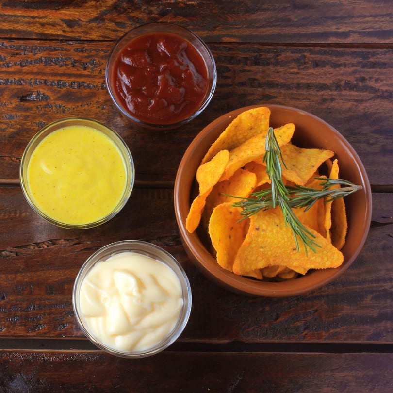 Nachos with rosemary in a bowl, with three dipping sauces: ketchup, mustard, and mayonnaise.