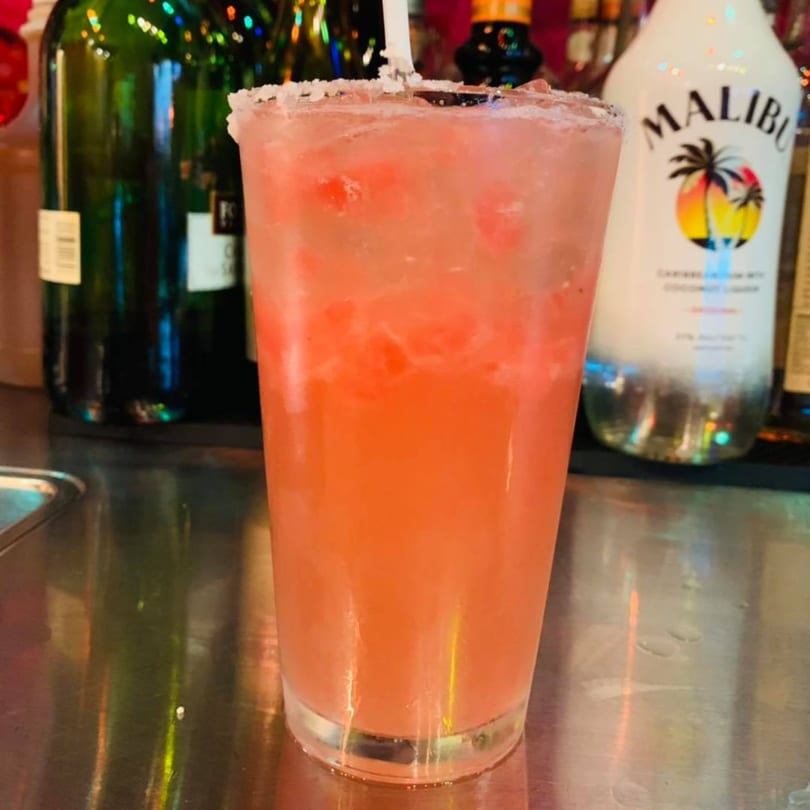 A vibrant pink El Sazón Bar & Grill margarita with a salted rim and straw, on a bar.